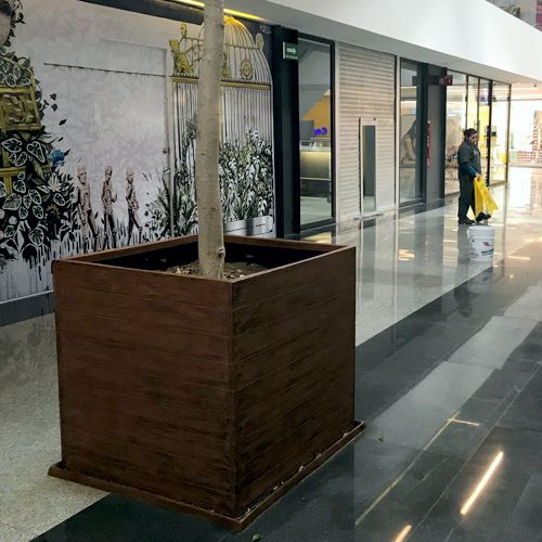 Maceta de fibra de vidrio imitacion madera en forma de cubo en un centro comercial